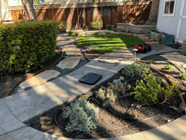 Construction phase of a backyard retaining wall with tools and materials visible, showing progress in landscaping.